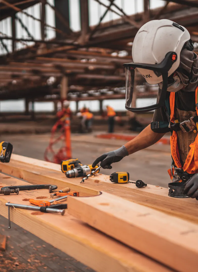 Carpenter in safety gear measuring structural timber on site